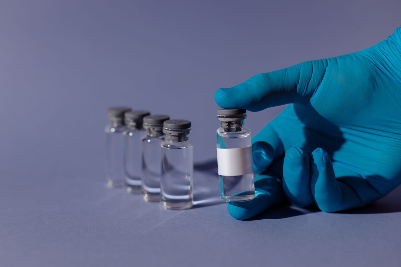 about-us Blue-gloved hand holding a transparent vial with liquid, representing healthcare and vaccination.